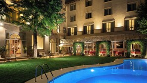 A hotel courtyard with a swimming pool, outdoor seating, and a covered dining area.