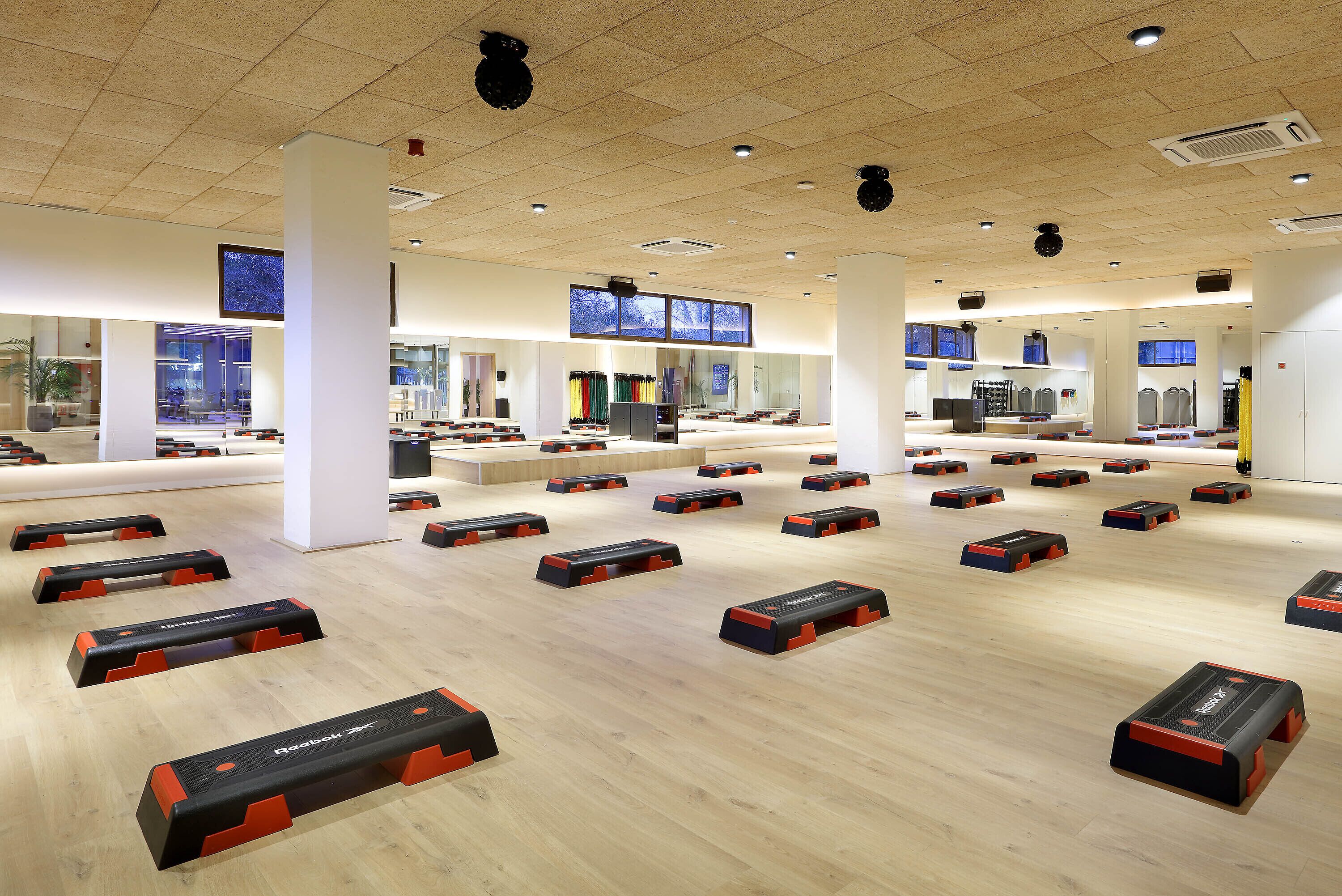 A spacious room with multiple exercise stations arranged on the floor, large windows, and a high ceiling with recessed lighting.