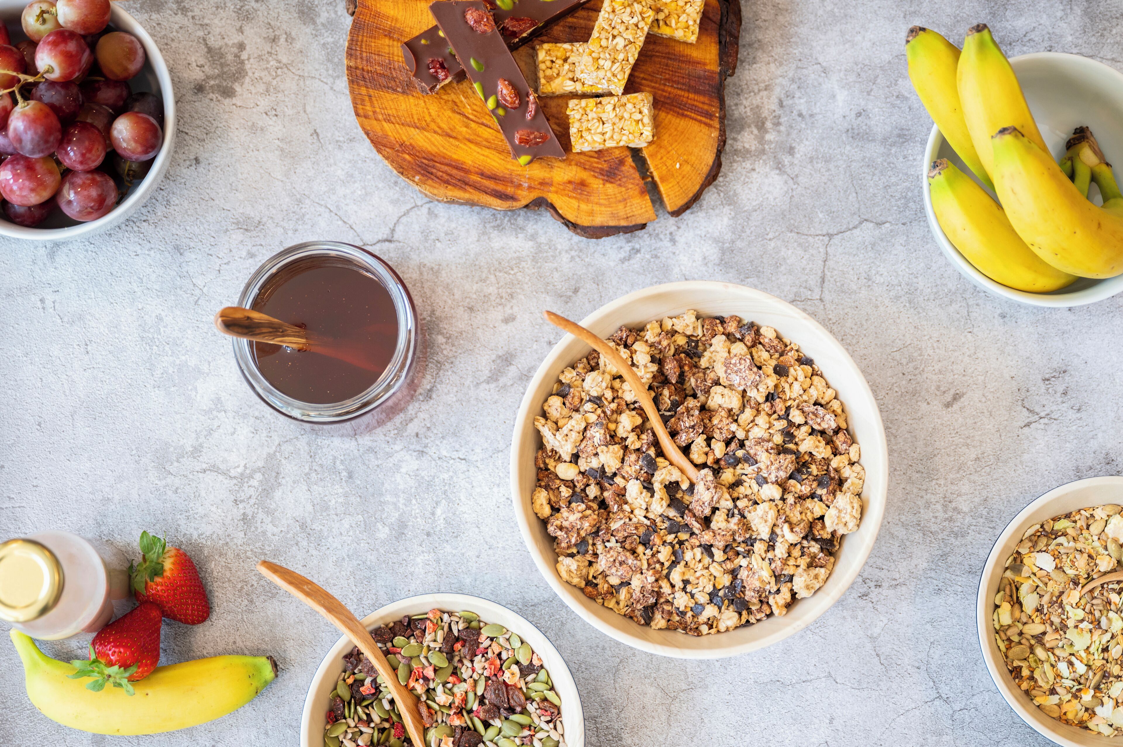 Variedad de alimentos como uvas, plátanos, granola y barras de chocolate dispuestas sobre una mesa.