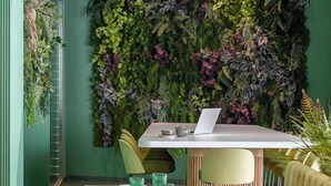 A restaurant with a long wooden table set for dining, a laptop on the table, and a green wall with plants behind it. - Hesperia Sant Just (Sant Just Desvern)