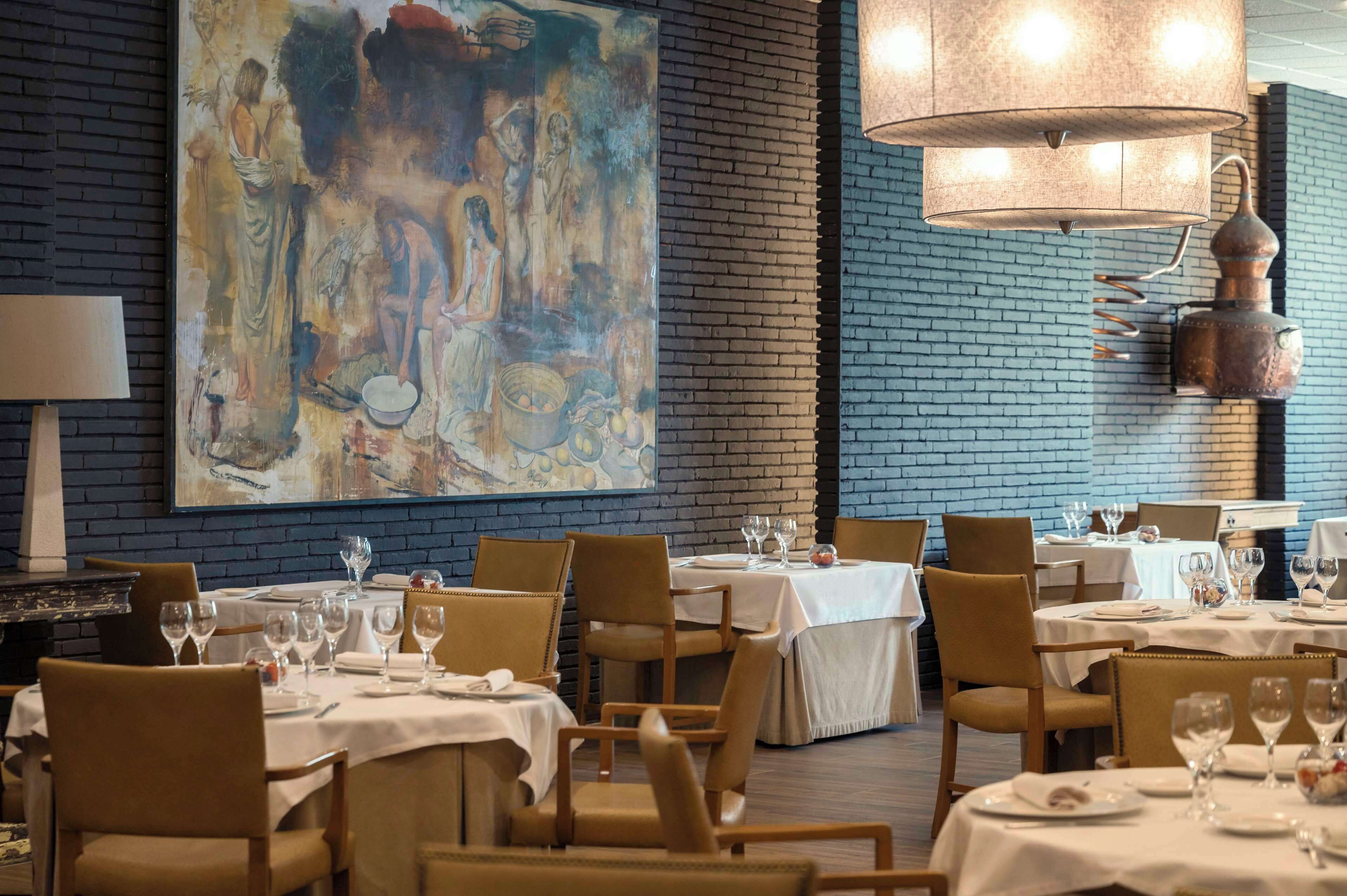 A restaurant with tables set for dining, a large abstract painting on the wall, and a copper distillery on the right.