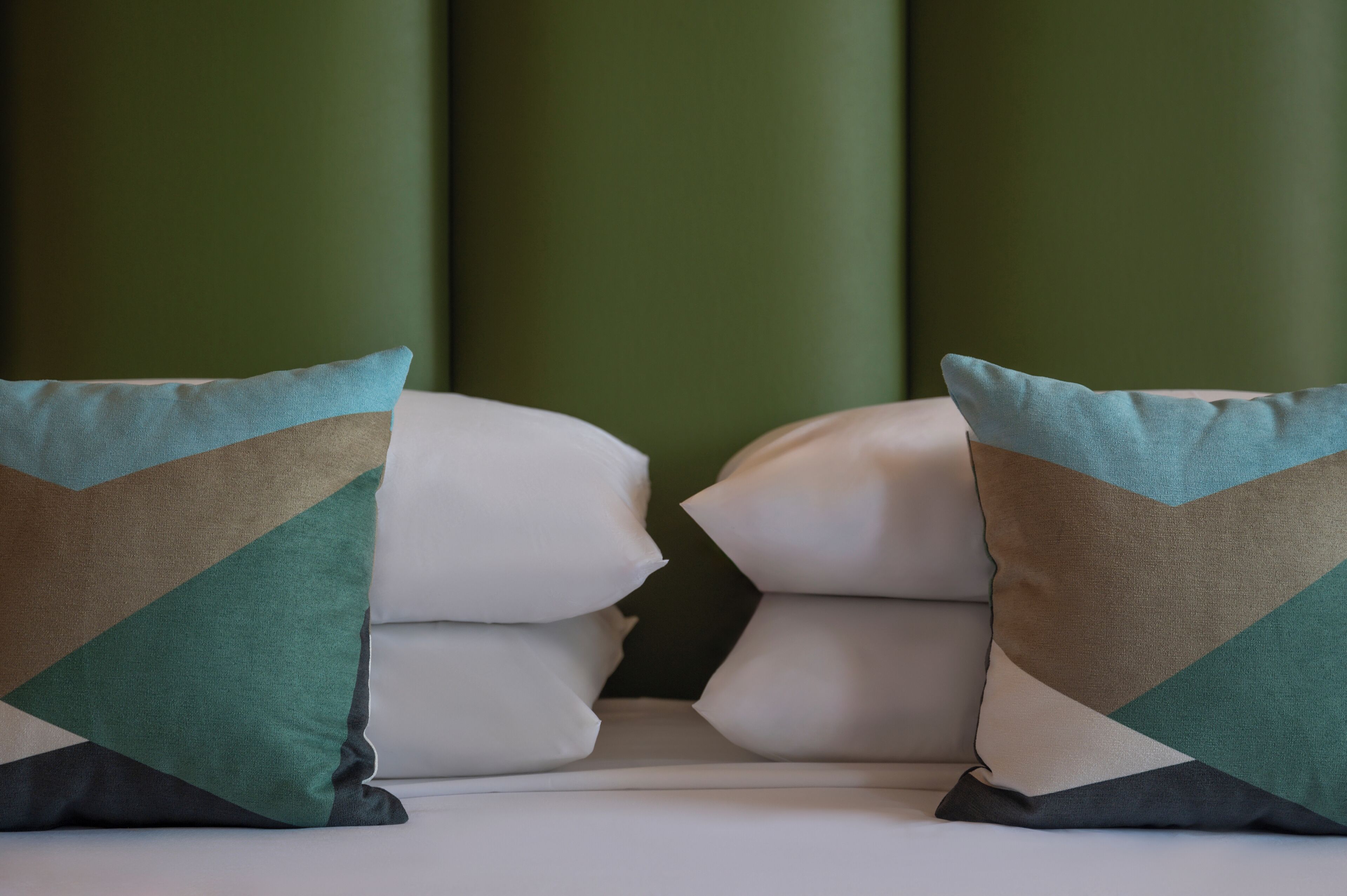 A bed with two pillows, a green wall, and a white headboard.