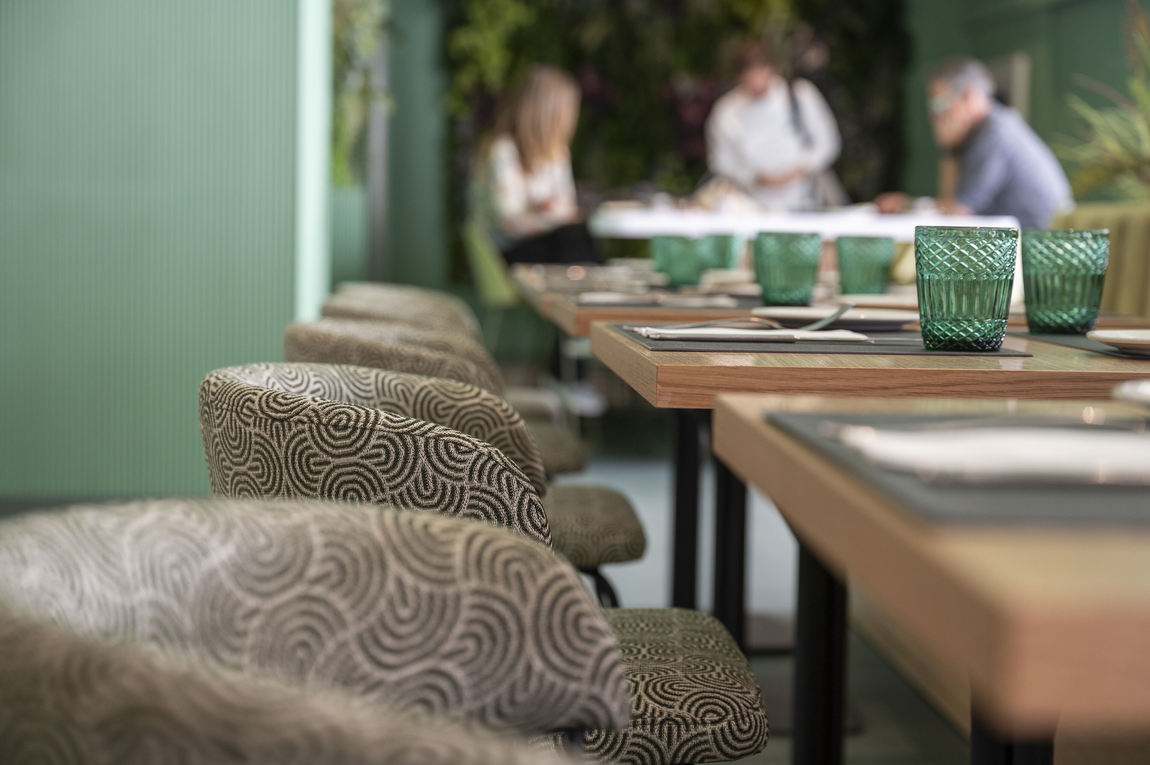 Un restaurante con sillas tapizadas de estampado y vasos verdes sobre las mesas.