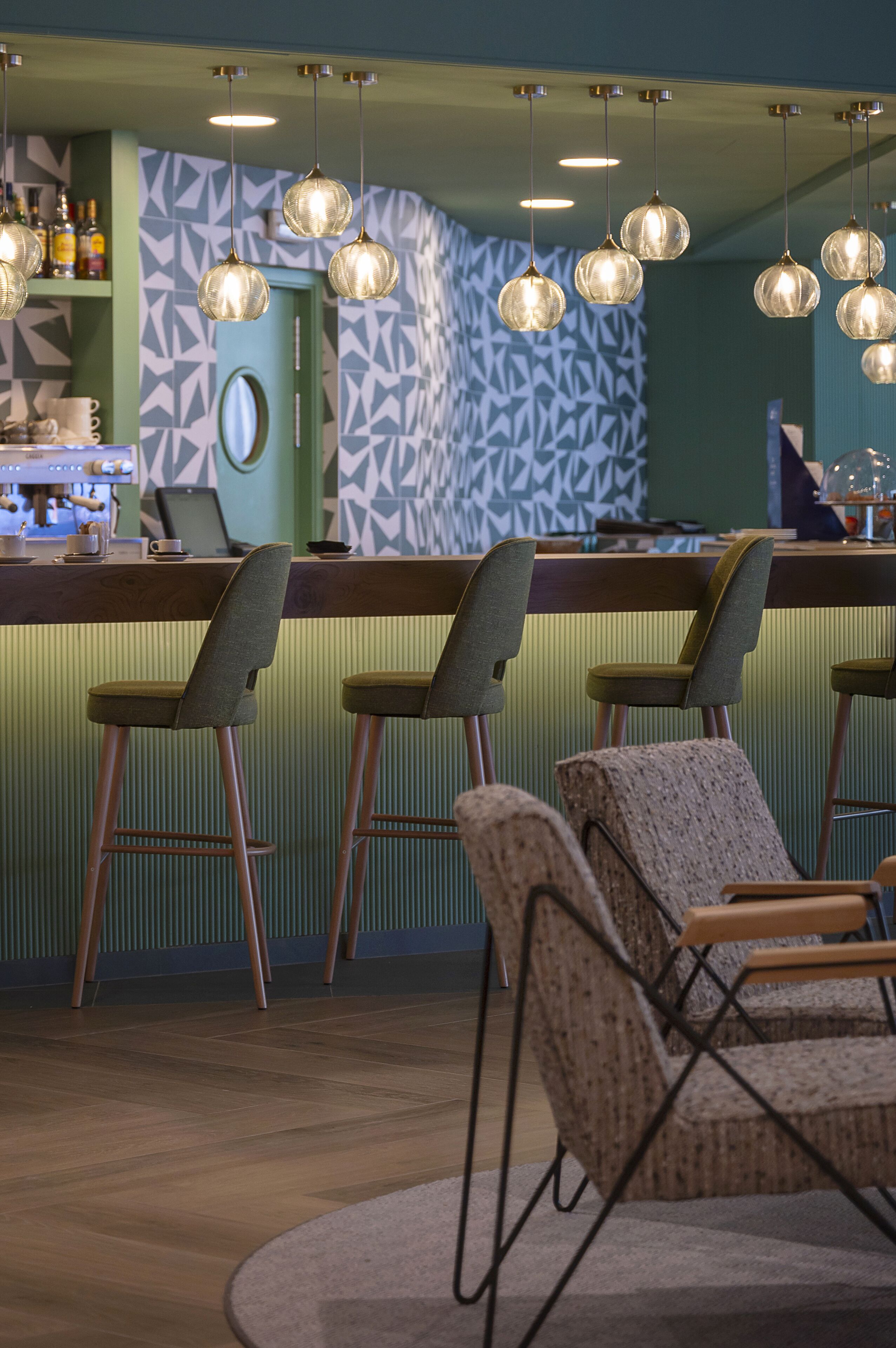 A bar area with multiple hanging light fixtures, bar stools, and a counter with a laptop and various items.