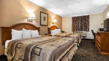 A hotel room with two beds, a desk, a television, and a window with curtains.