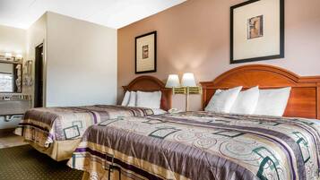 A hotel room with two beds, a wooden headboard, a mirror, and framed pictures on the wall.
