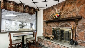 A cozy interior with a stone fireplace, a dining area with chairs, and a view of a stone wall through a window. - Quality Inn & Suites Binghamton Vestal (Binghamton)