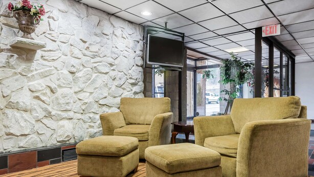 A lobby with a stone wall, a TV mounted on the wall, and three yellow armchairs with ottomans. - Quality Inn & Suites Binghamton Vestal (Binghamton)