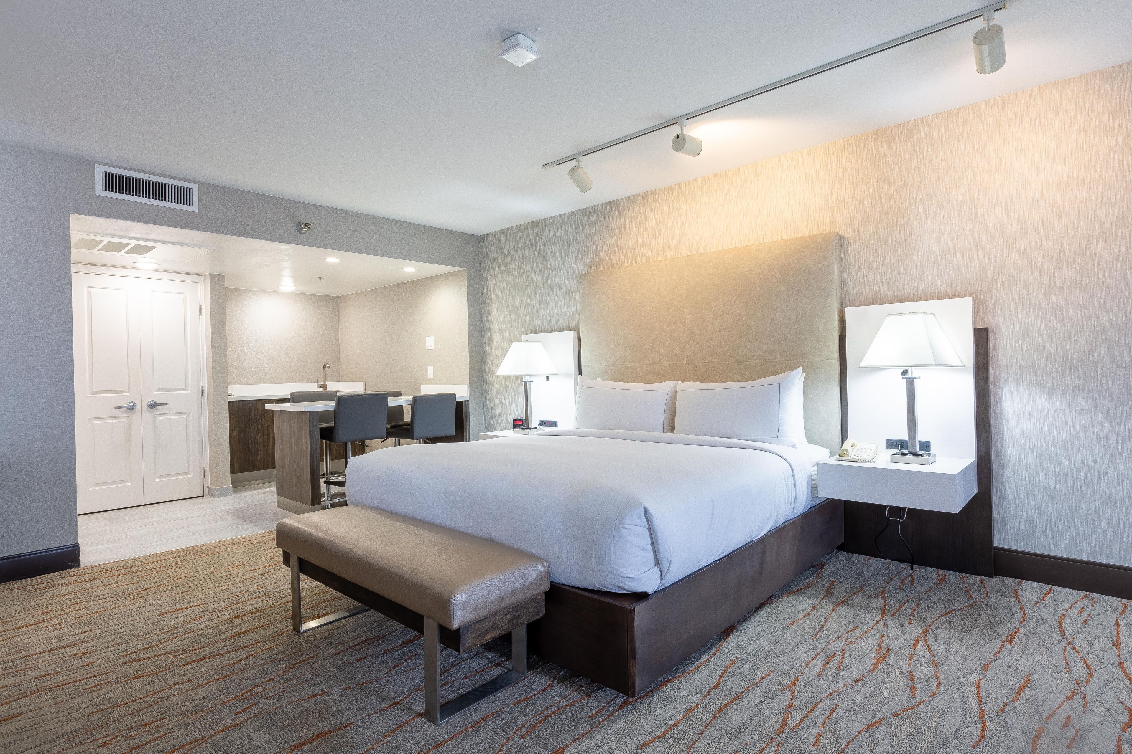 Una habitación de hotel con una cama grande, mesitas de noche, un escritorio y un banco.