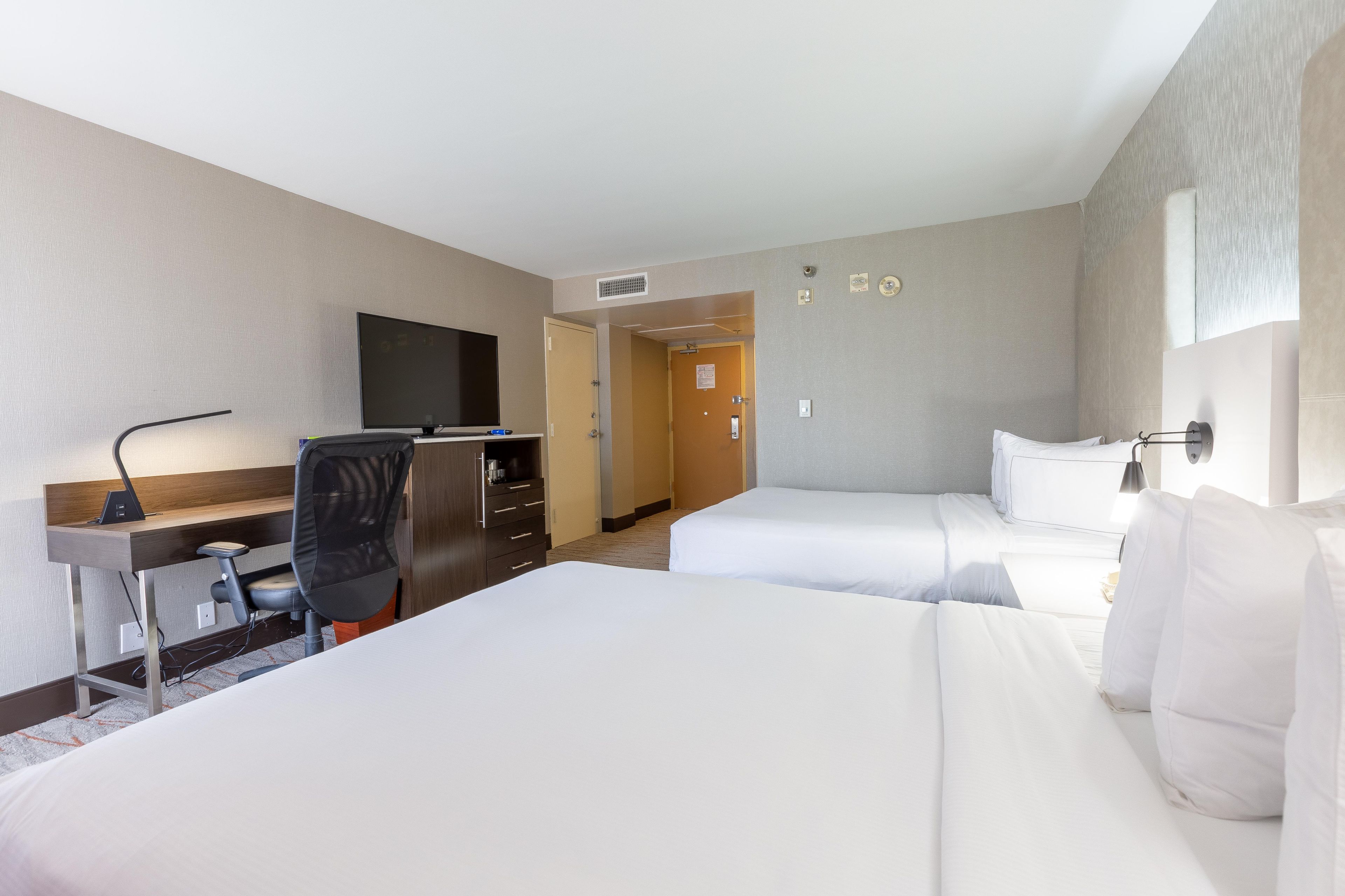 Habitación de hotel con dos camas, un escritorio con silla, televisor y puerta que da a otra habitación.