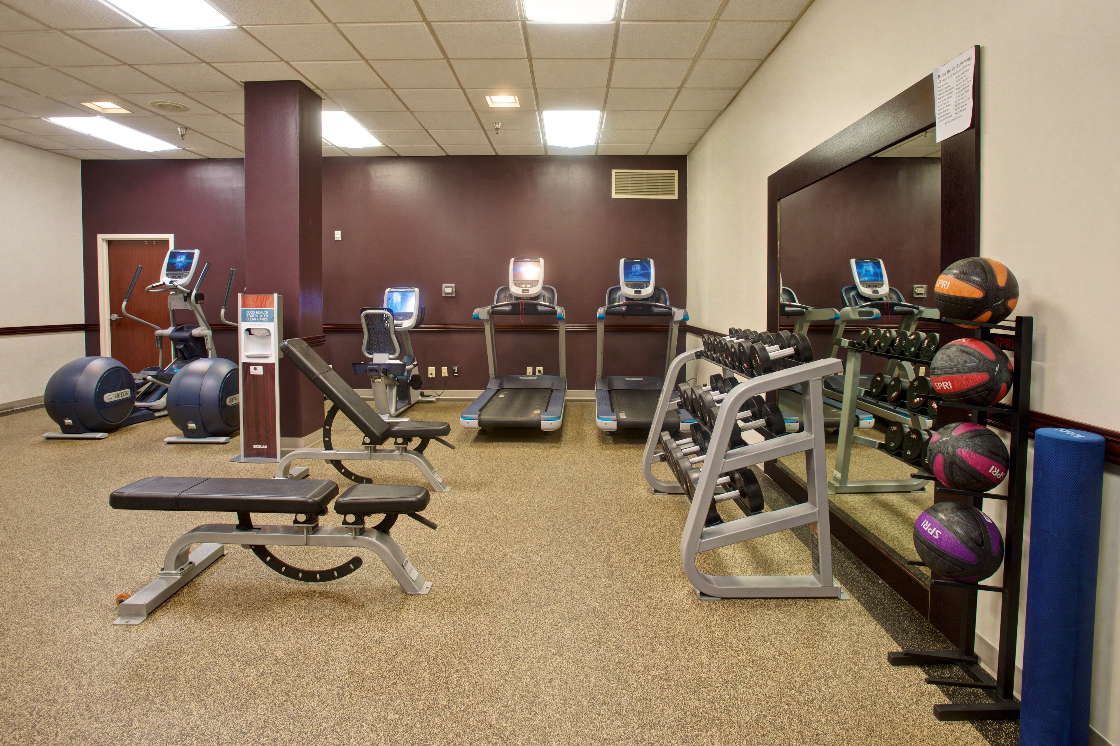 A gym with treadmills, elliptical machines, weight benches, and various exercise balls.
