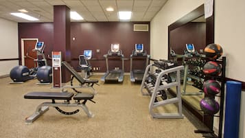 A gym with treadmills, elliptical machines, weight benches, and various exercise balls.