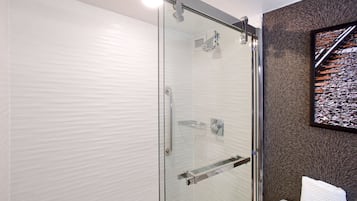 A modern bathroom with a glass shower enclosure, a toilet, and a mounted television.