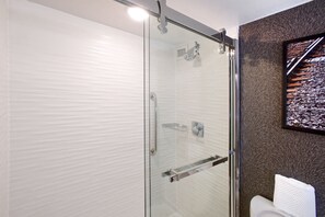 A modern bathroom with a glass shower enclosure, a toilet, and a mounted television. - DoubleTree by Hilton Dallas - Richardson (Richardson)
