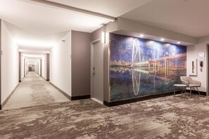 Ein Hotelgang mit Teppichboden, einer großen Wandmalerei einer Brücke und einem Sessel.