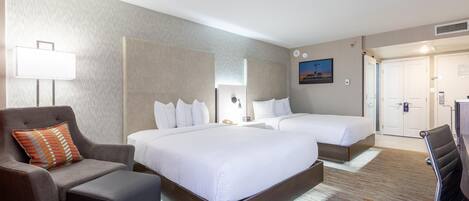A hotel room with a large bed, a smaller bed, a sofa, a desk, and a chair. There is a painting on the wall and a window with blinds.