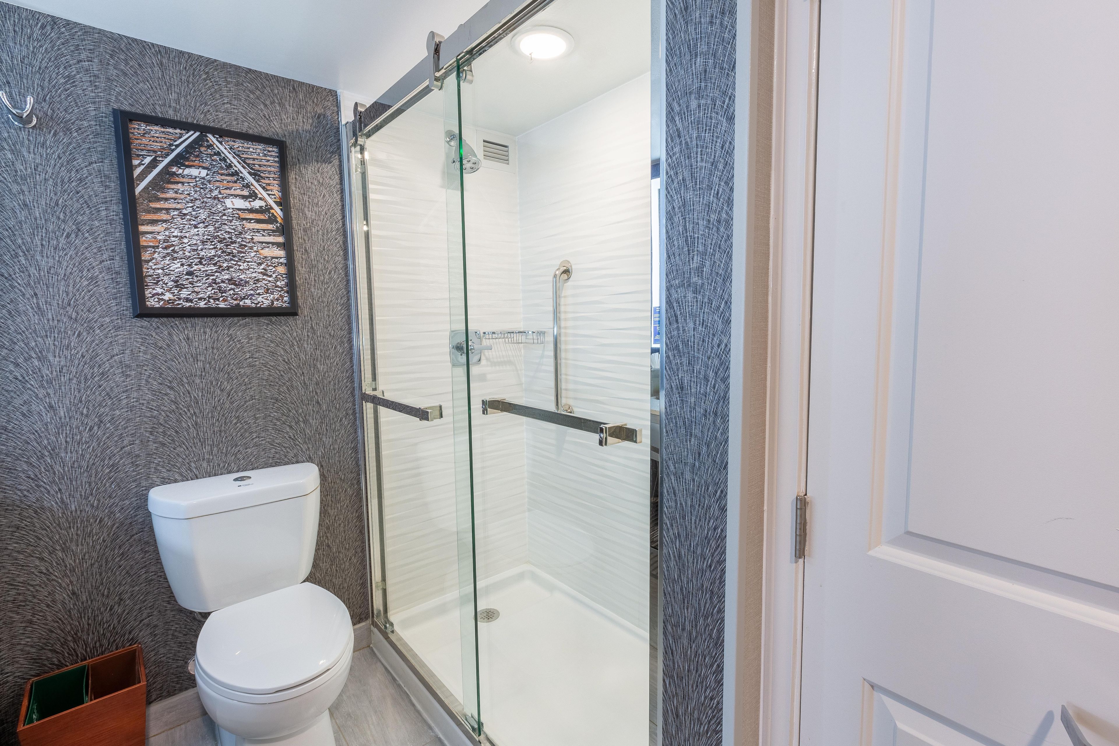 Un baño con inodoro, cabina de ducha de vidrio y un cuadro en la pared.