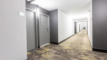 Un pasillo de hotel con puertas, suelo alfombrado y una lámpara en el techo.