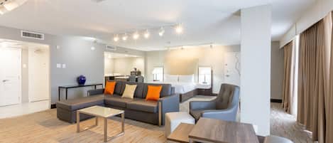 A modern hotel room with a sofa, chairs, a small table, and a bed.