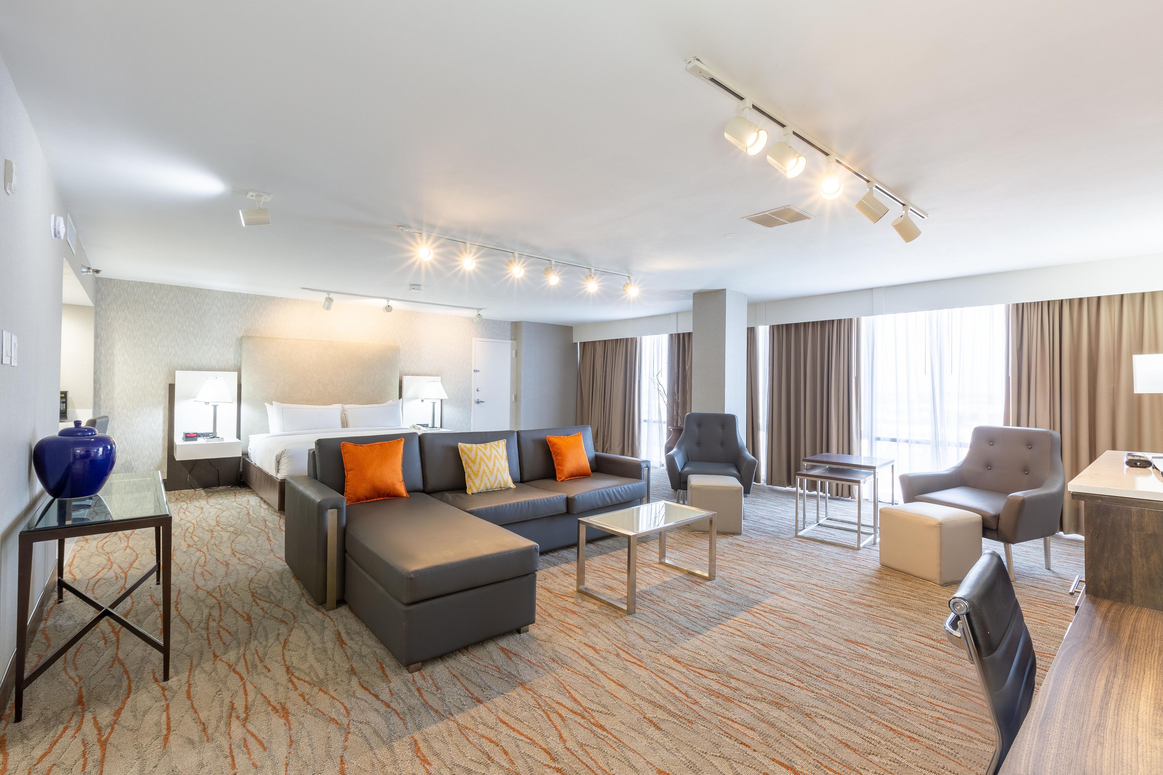 A hotel room with a sofa, armchairs, a coffee table, a desk, and a bed.