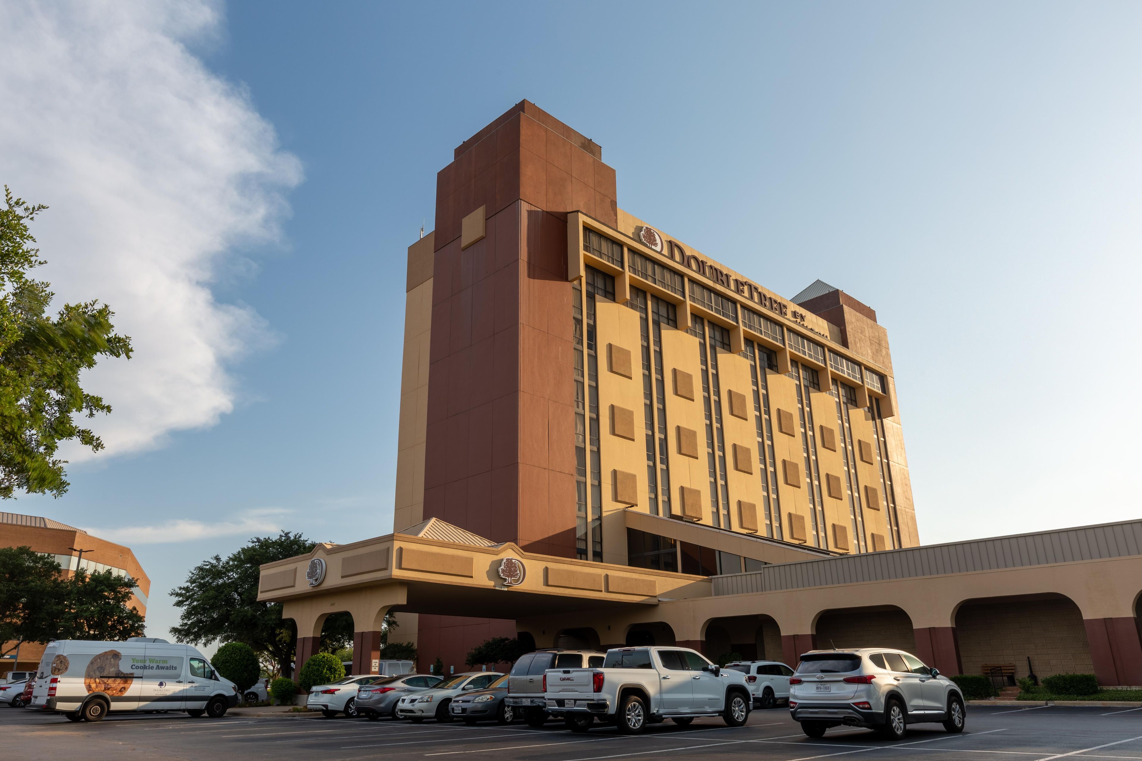 Un hotel con diseño moderno, que destaca por su entrada principal y cuenta con varios espacios de estacionamiento.