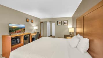 A hotel room with a large bed, a desk with a television, a microwave, and a door leading to another room.
