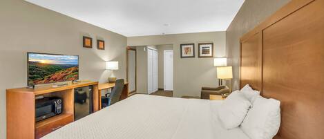 A hotel room with a large bed, a desk with a television, a microwave, and a door leading to another room.