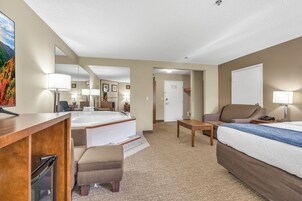 Habitación de hotel con cama, escritorio, silla, mesita, sofá, baño con bañera y un espejo grande.