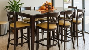 A dining area with a glass table surrounded by six wooden chairs with yellow cushions. A potted plant is on the left, and a vase with flowers is on the table. - Bristol Arcadia Inn (Bristol)