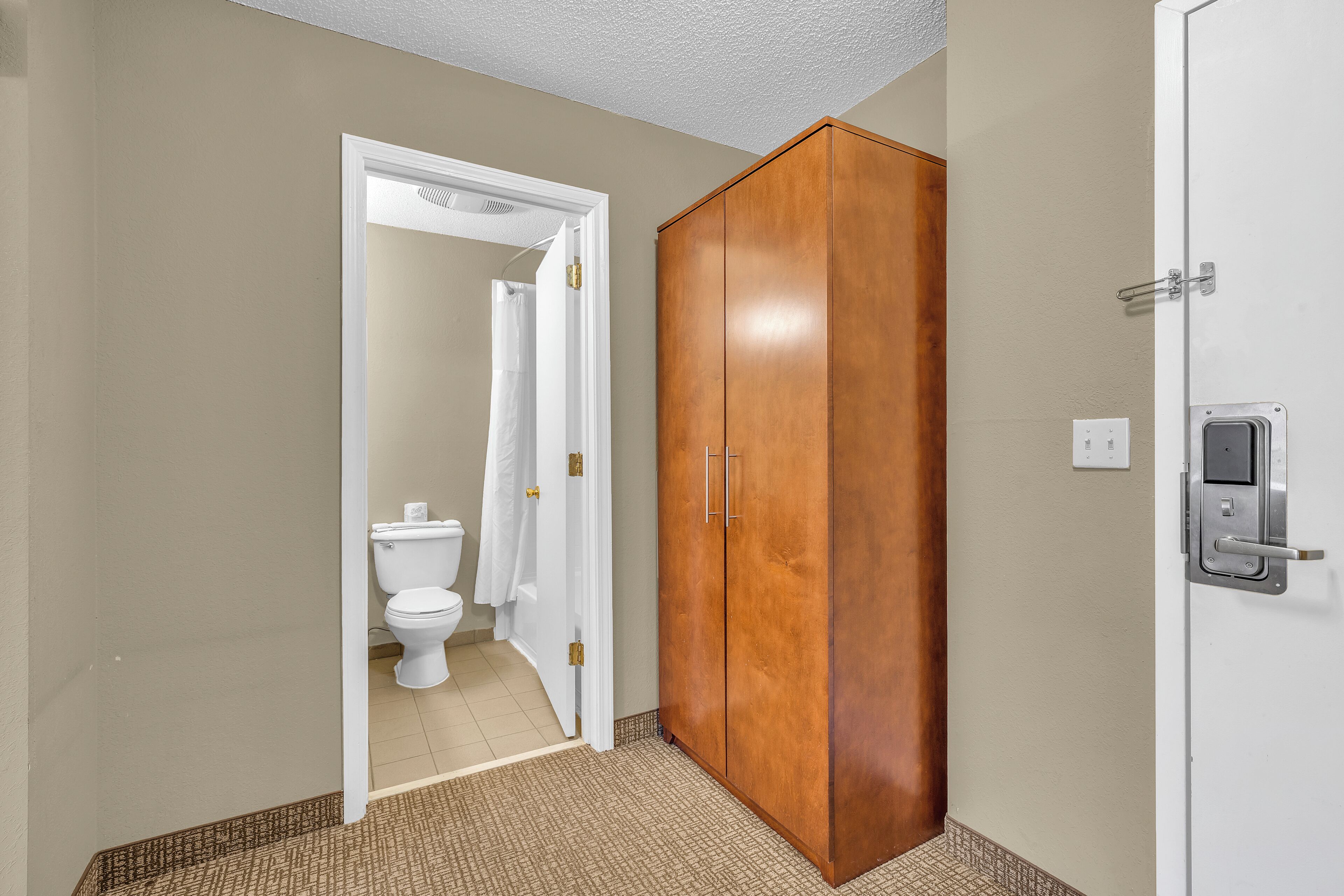 A bathroom with a toilet, a white shower curtain, and a wooden wardrobe with two doors.