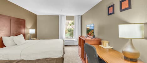 Habitación de hotel con cama, escritorio, silla, lámpara y dos cuadros en la pared.