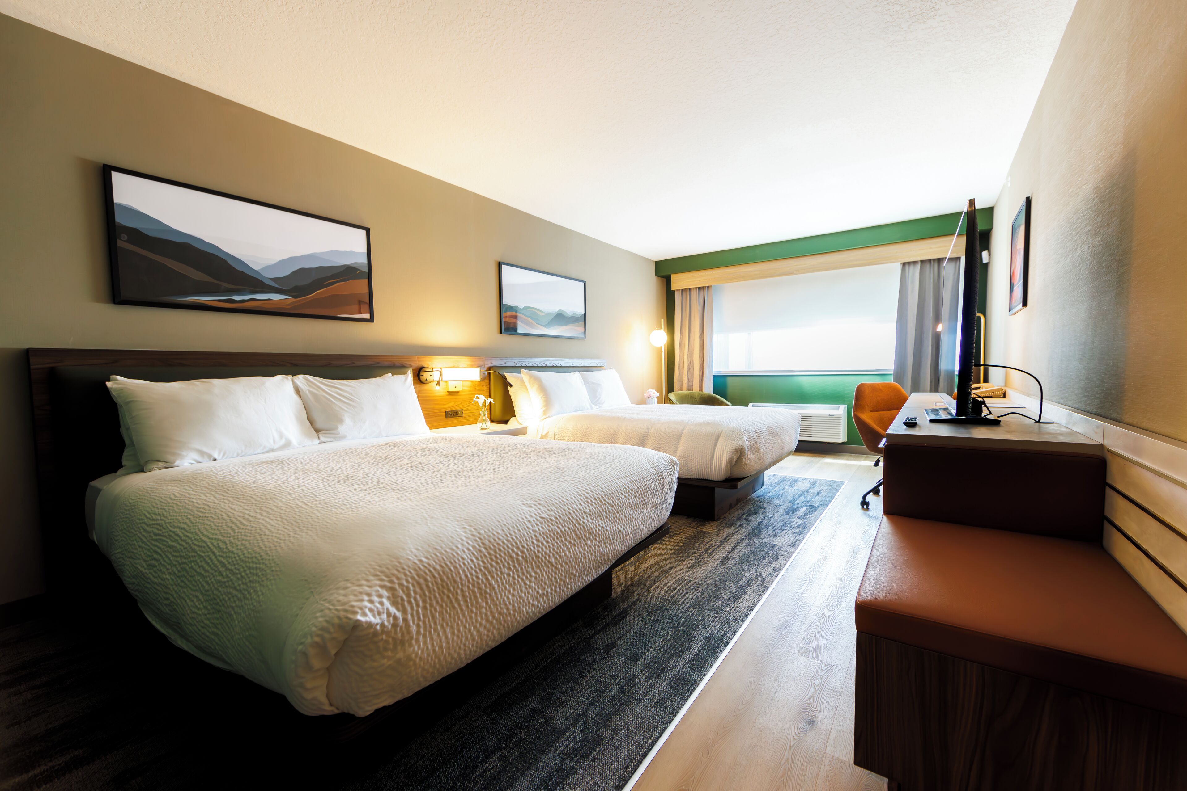 Habitación de hotel con dos camas, un escritorio y vistas al exterior.