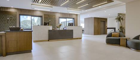 A modern hotel reception area with a reception desk, seating area, and a large window providing natural light.