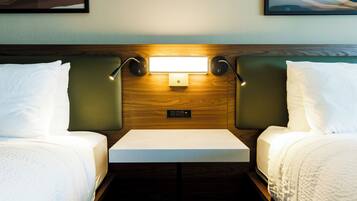 A hotel room with two beds, a bedside table, and a wall-mounted light fixture.