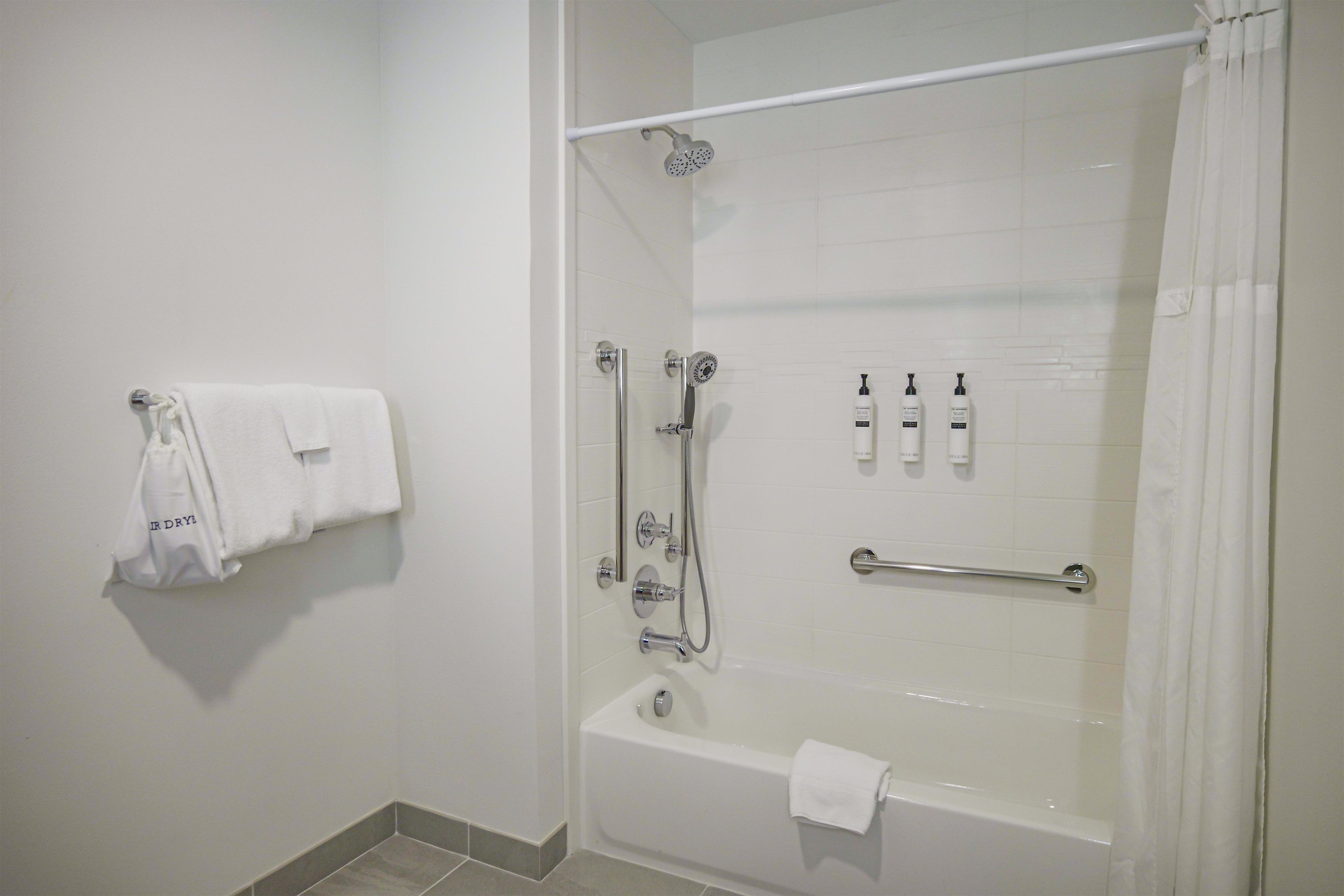 A modern bathroom with a bathtub, shower, and handrails.