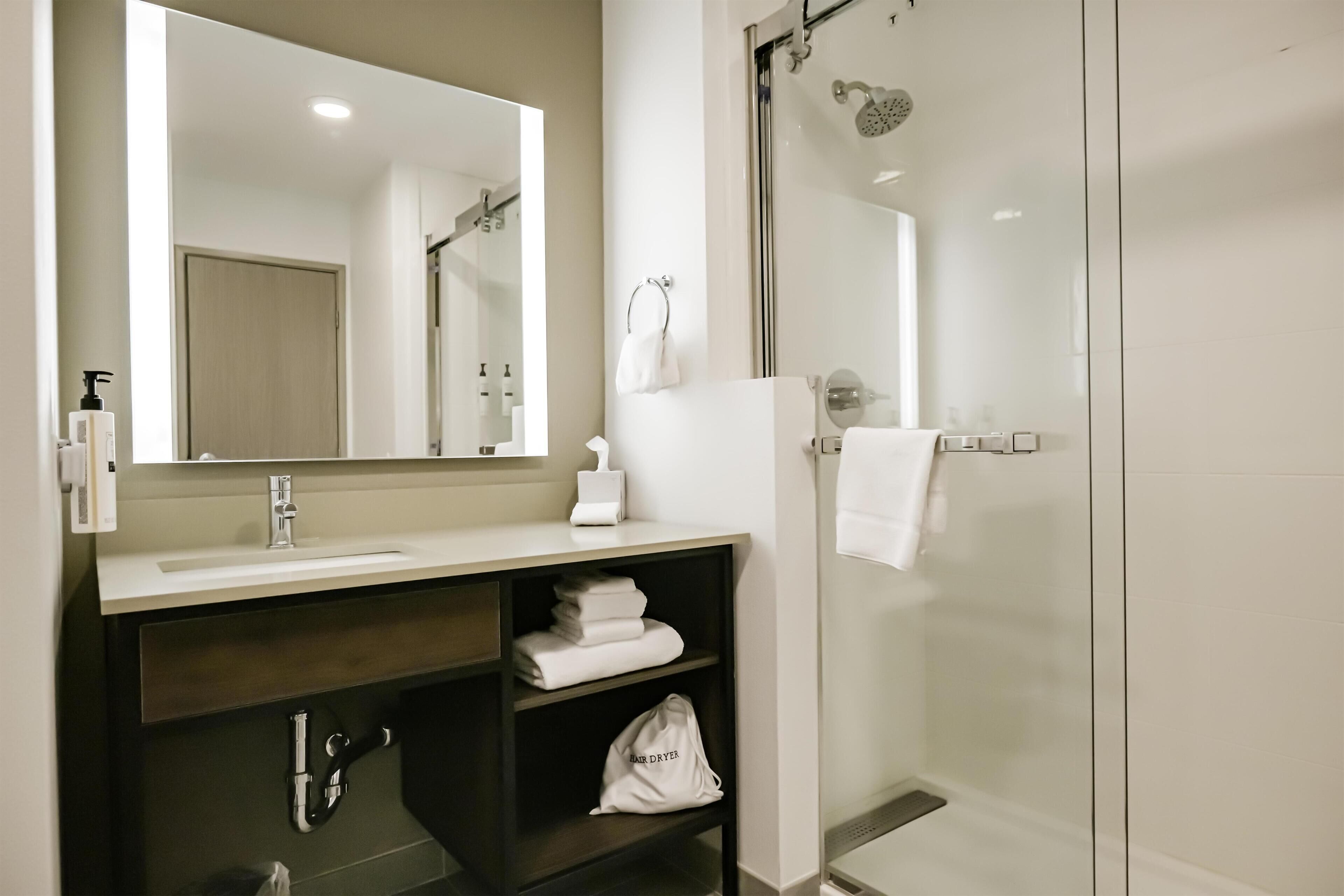 Un baño moderno con lavamanos, espejo, toallero y ducha con mampara de vidrio.