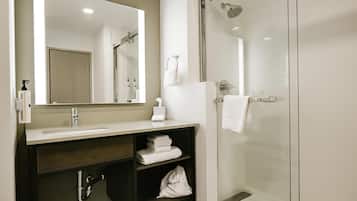 Un baño moderno con lavamanos, espejo, toallero y ducha con mampara de vidrio.