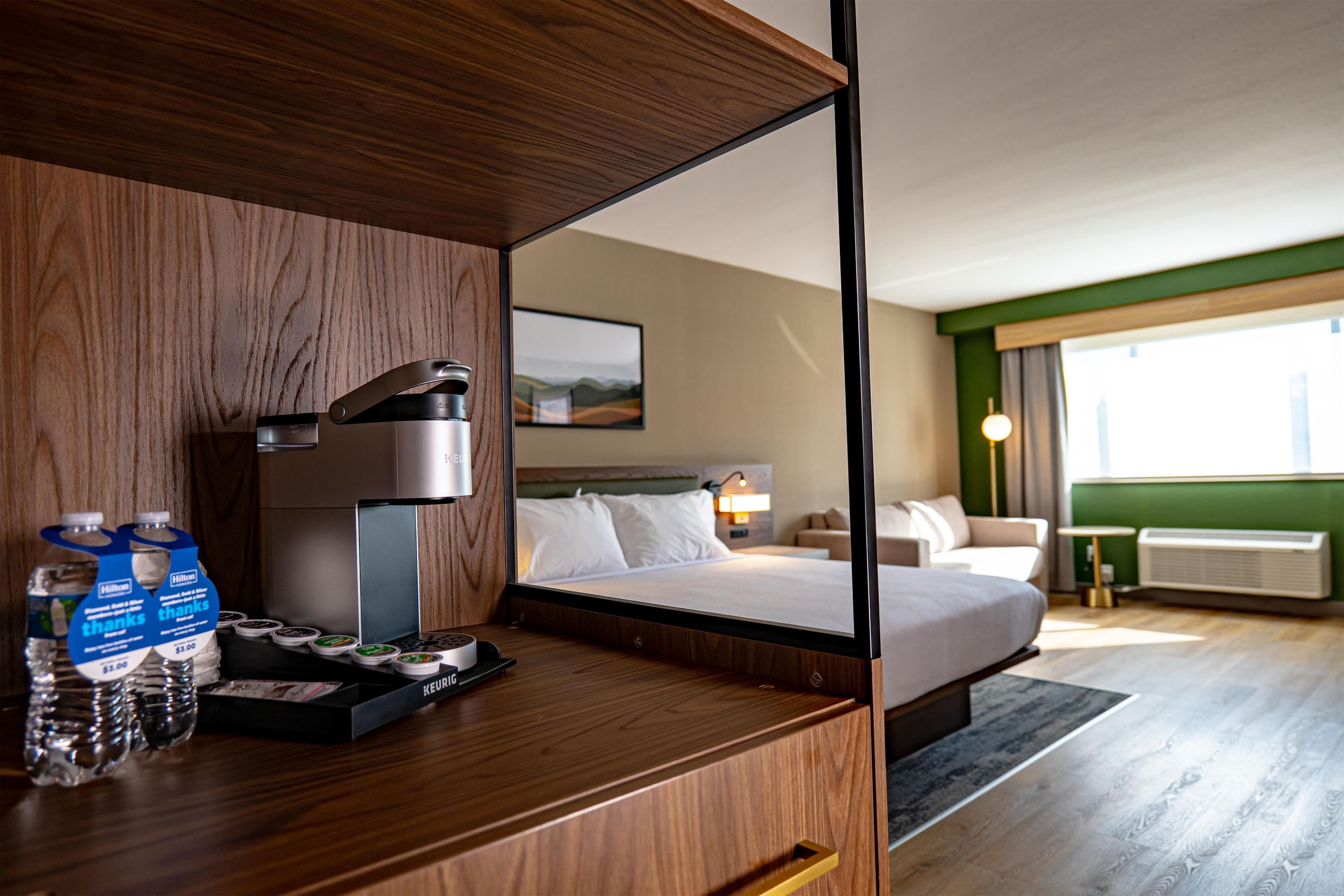 Une chambre d’hôtel avec un bureau en bois, un minibar et un lit donnant sur le paysage urbain.