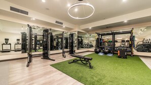 Une salle de sport équipée de matériel d’exercice, dotée d’un espace recouvert d’une moquette verte et d’un grand miroir.