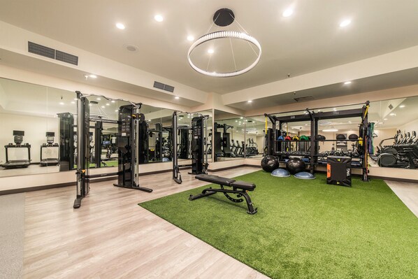 A gym with exercise equipment, a green turf area, and a large mirror.