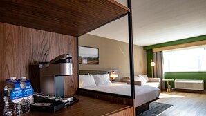 Une chambre d’hôtel comprenant un lit, une table de chevet avec un miroir, une commode, un bureau avec un ordinateur et une fenêtre donnant sur l’extérieur.
