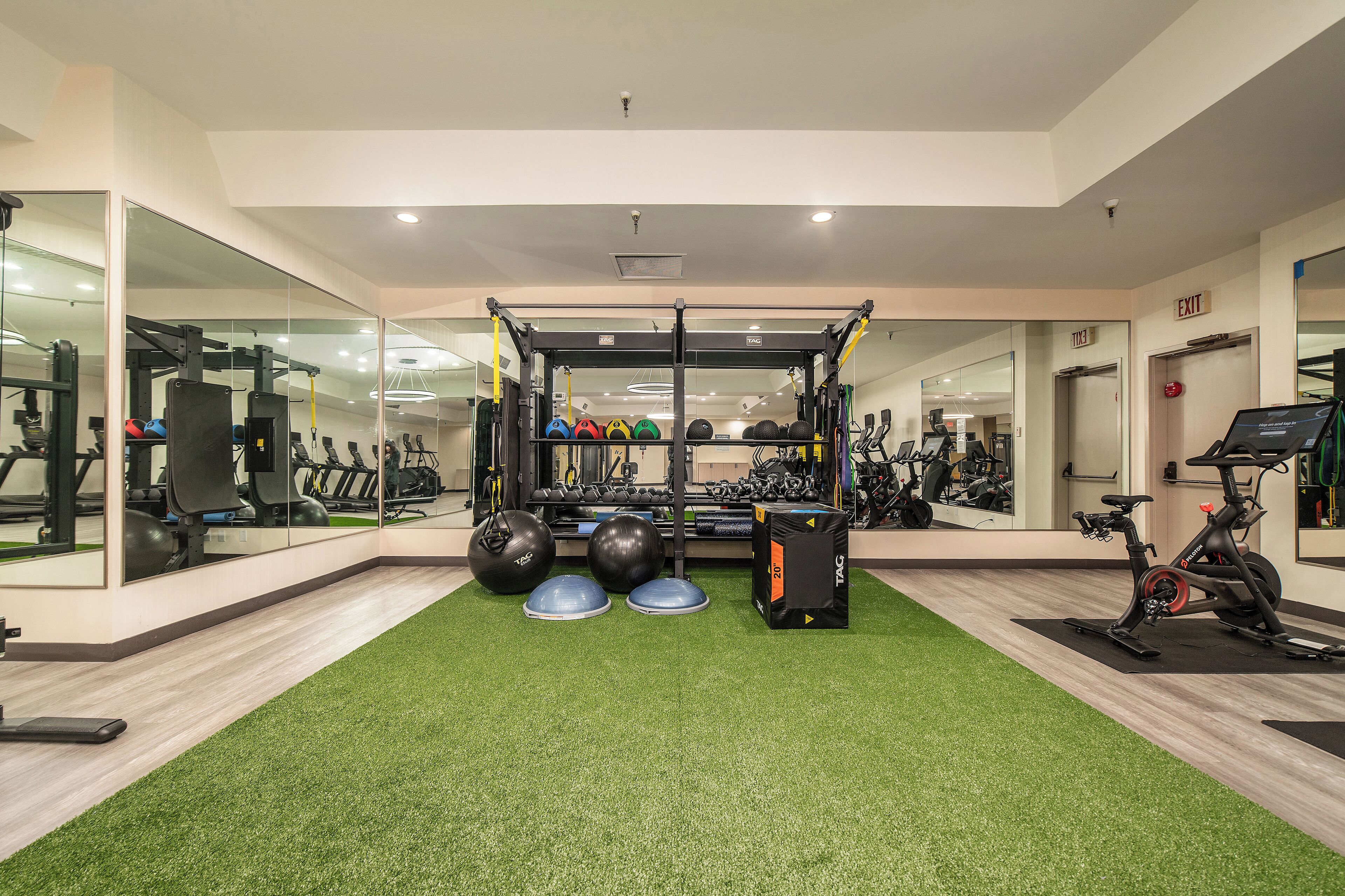 A gym with exercise equipment, a mirrored wall, and a green carpet.