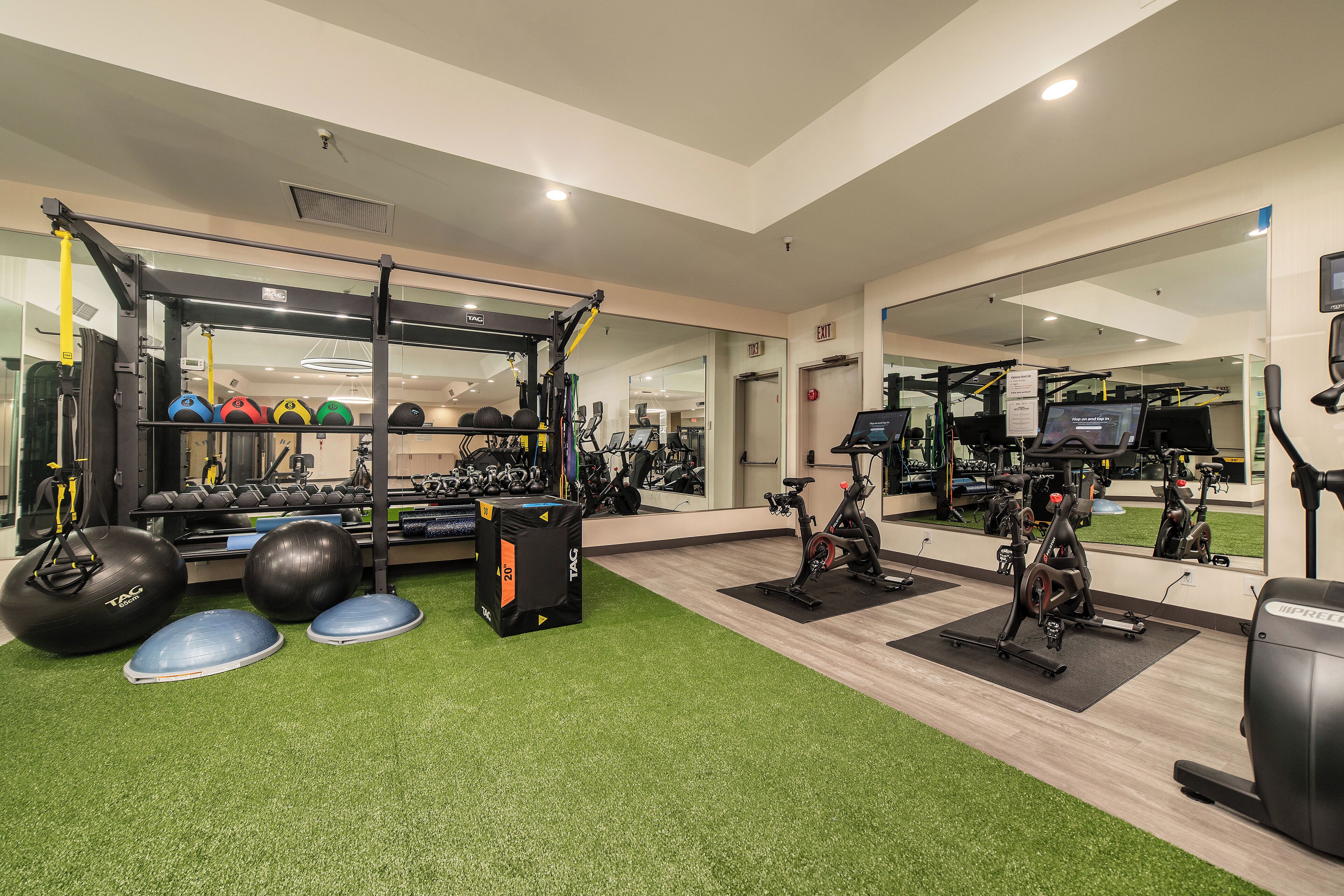 A gym with exercise equipment, a mirror, and a green artificial turf floor.