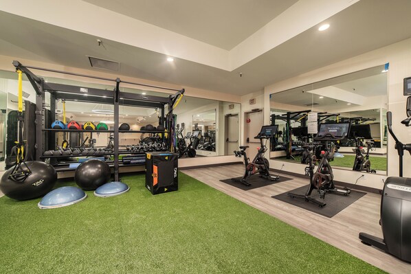 A gym with exercise equipment, a mirror, and a green artificial turf floor.