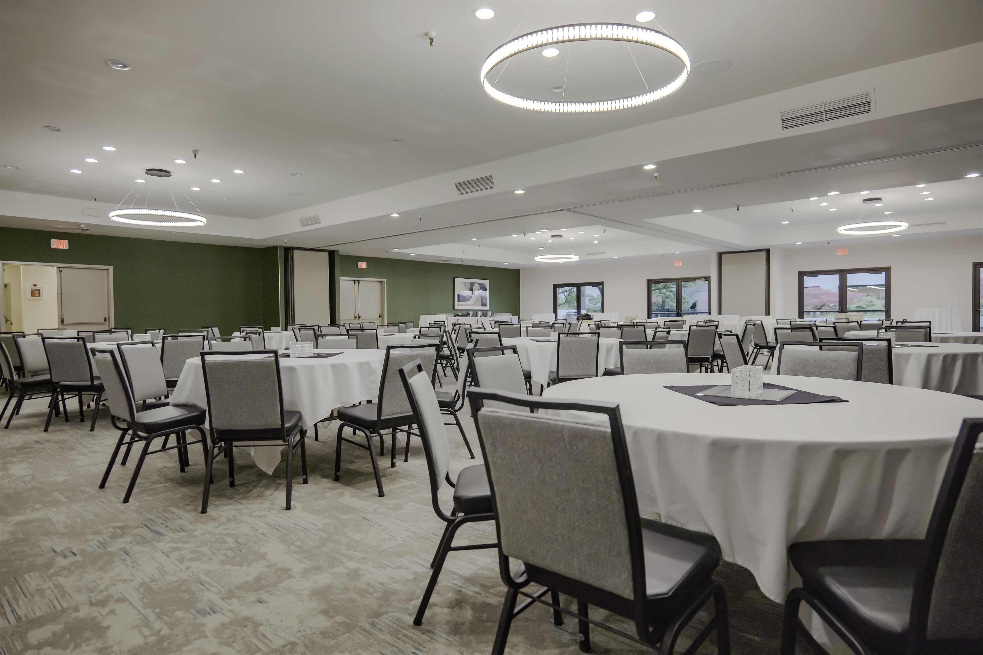 Un salón de conferencias con mesas y sillas redondas, equipado con luces en el techo y ventanas.