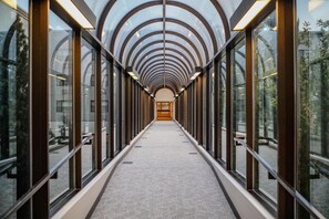 A corridor with a glass ceiling and walls, leading to a central area with a door.