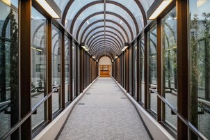 Un pasillo con techo y paredes de vidrio, que conduce a una zona central con una puerta.