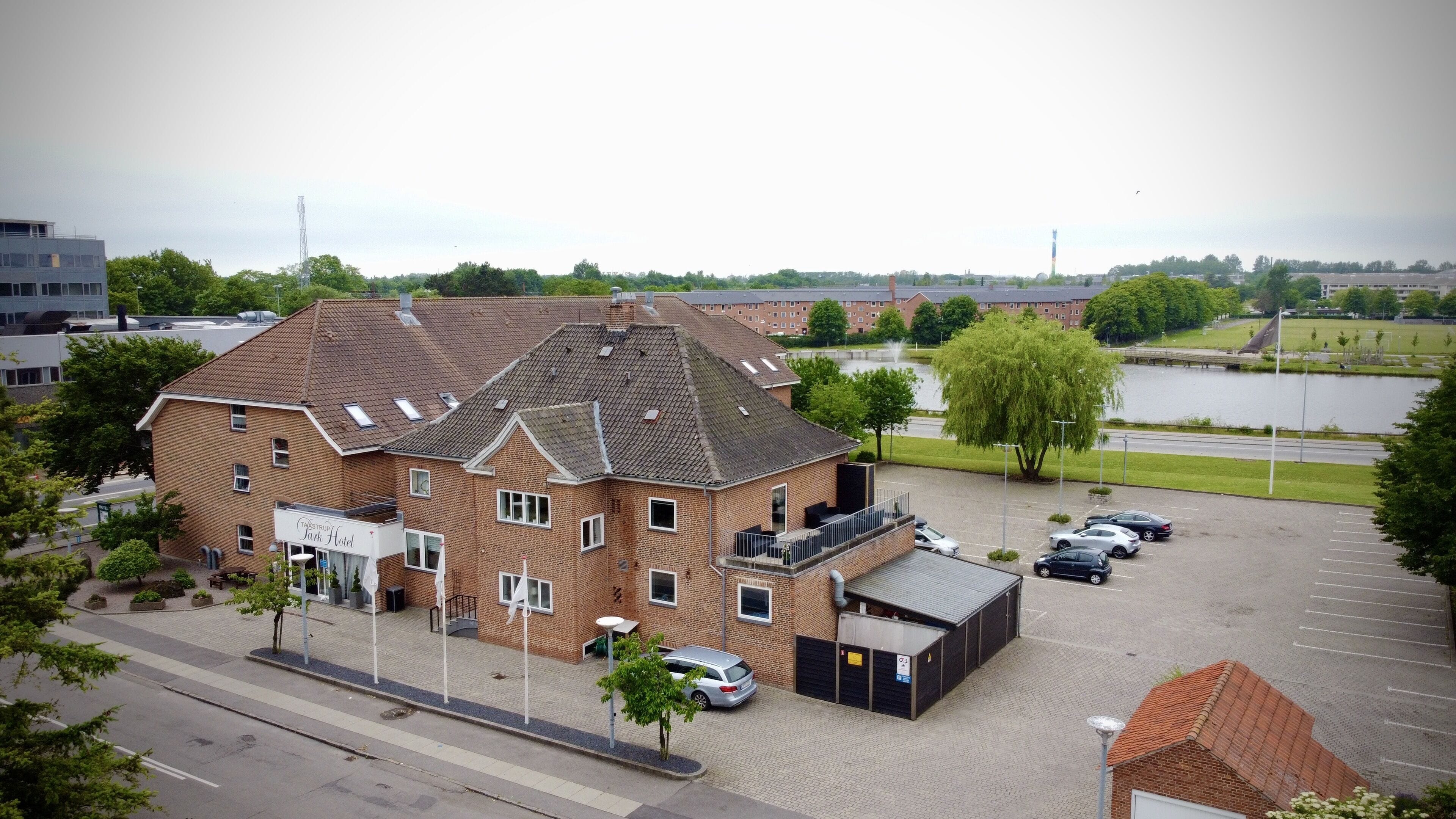 En byggnad av tegel med en skylt som visar texten ”Jans Hotel” och en parkeringsplats med flera bilar.