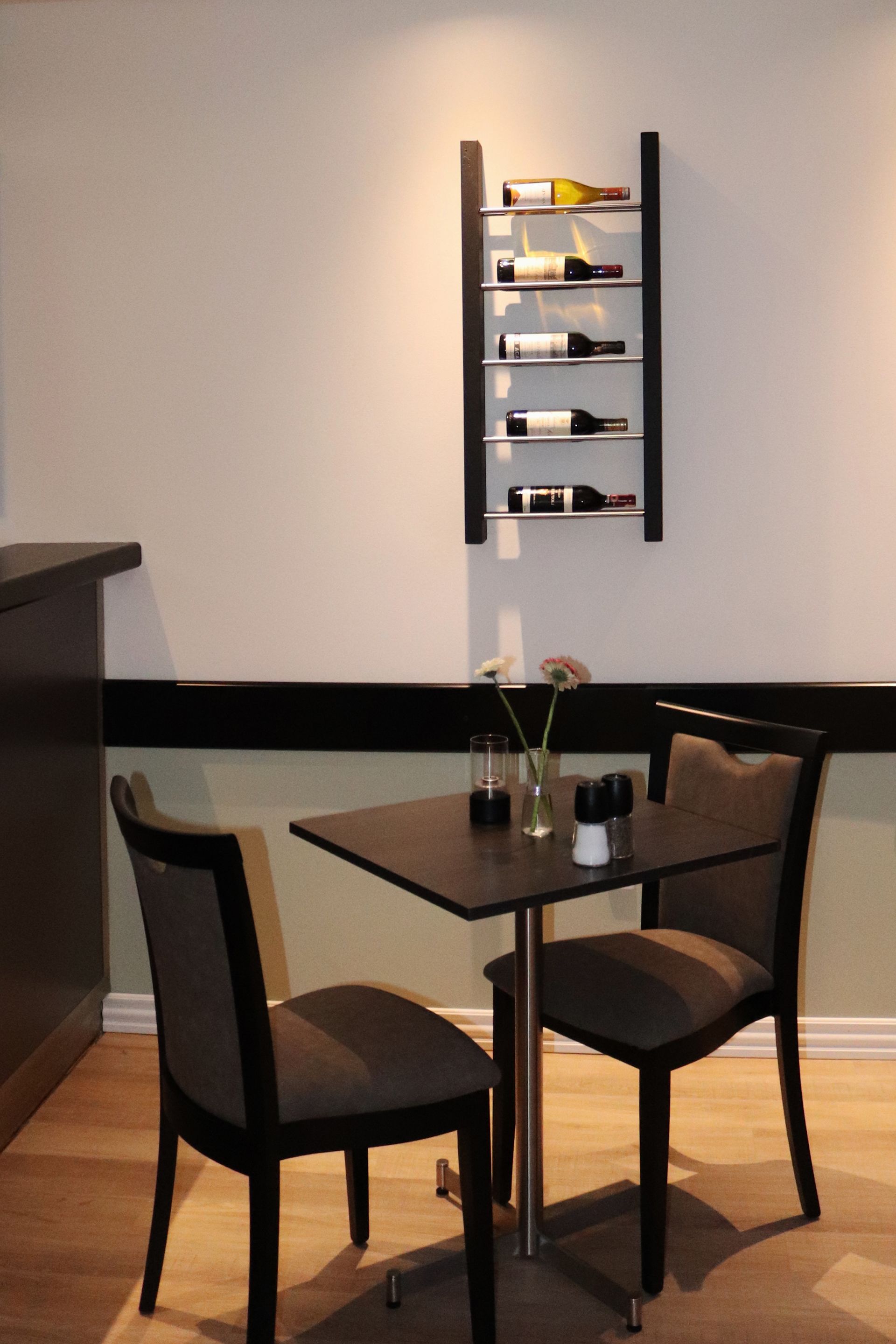 Un espace repas moderne avec une table et des chaises en bois foncé, un meuble à vin fixé au mur et un vase rempli de fleurs sur la table.