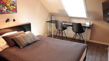 A bedroom with a large bed, a desk with two chairs, a radiator, and a window.